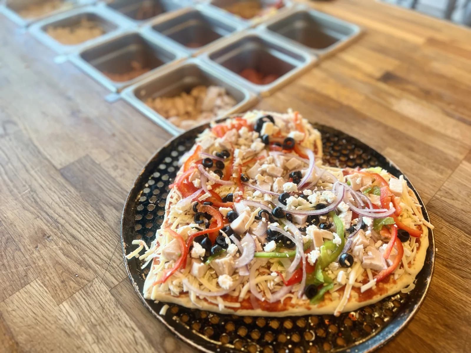 A pizza being built fresh with toppings from the prep line